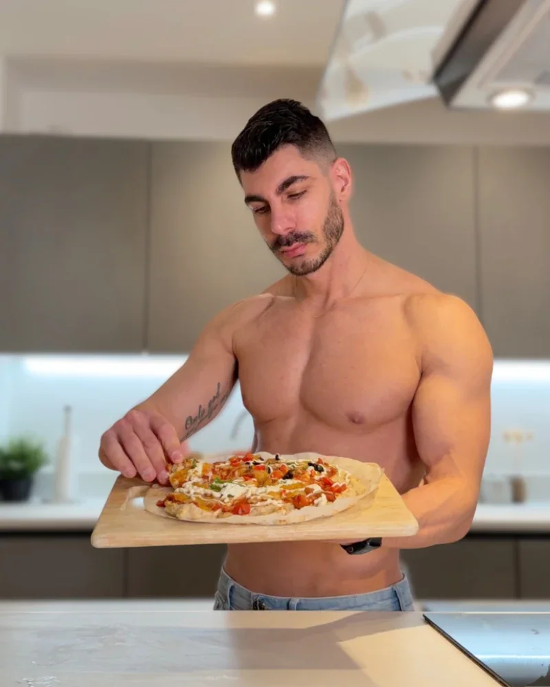 Atai holding a freshly prepared pizza in his kitchen